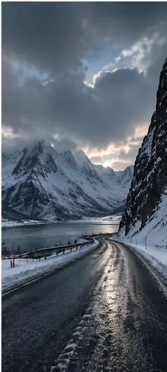 Verschneite norwegische Küstenstraße entlang eines Fjords mit hohen Bergen, dunklen Wolken und winterlicher Landschaft als Norwegen Hintergrundbild