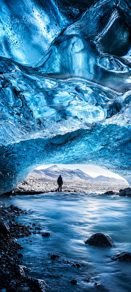 iPhone 18 Hintergrundbild mit blauer Eishöhle, Gletschersee, Eisformationen und verschneiten Bergen für iPhone 18 Pro und iPhone 18 Pro Max
