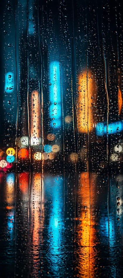 iPhone Regen Hintergrundbild mit Regentropfen auf einer Fensterscheibe und bunten Stadtlichtern bei Nacht.