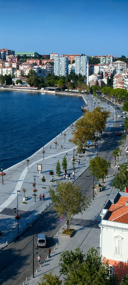 Moderne Küstenpromenade mit blauem Meer Stadtblick Bäumen und sonniger Uferstraße als helles Handy Hintergrundbild