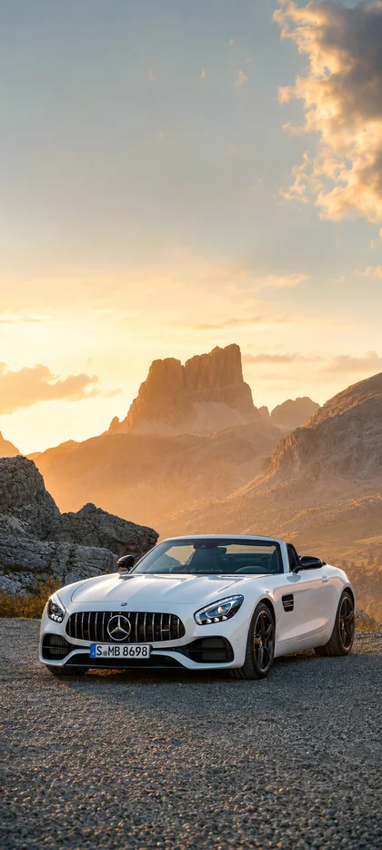 Weißer Mercedes AMG Roadster auf einer Bergstraße bei Sonnenuntergang mit felsiger Landschaft als vertikales Handy Wallpaper
